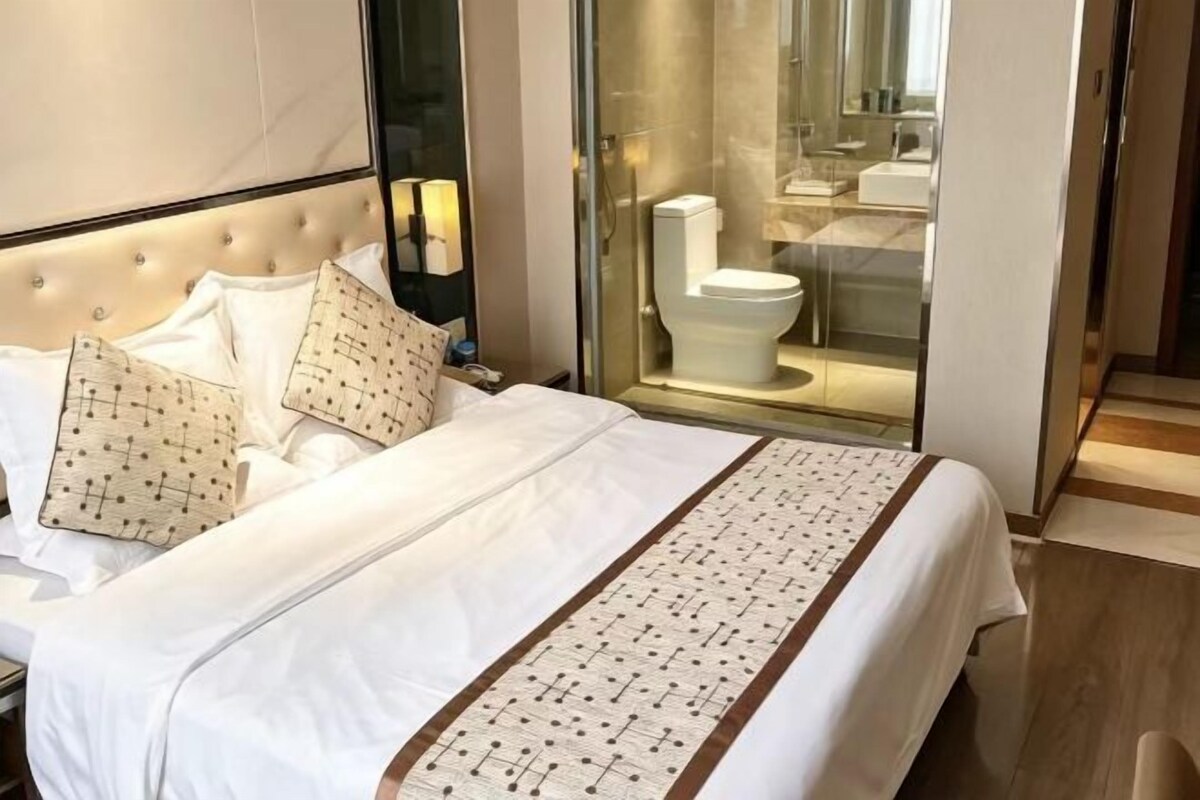 Habitación de hotel con cama, baño con paredes de vidrio y piso de madera.
