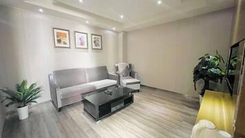 Una sala moderna con un sofá gris, un sillón blanco, una mesa de centro negra y una planta en maceta.