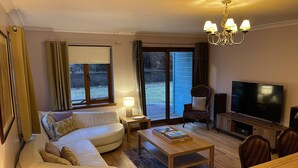 A living room with a sofa, coffee table, TV, and a dining area with chairs. - Foxglove Cottages (Drymen)