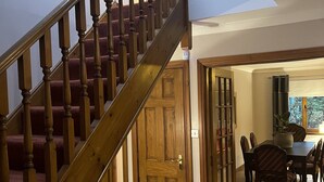 A wooden staircase with a red carpet leading to a dining area with a table and chairs. - Foxglove Cottages (Drymen)