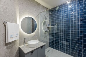 A modern bathroom with a round mirror, a white sink, and a glass-enclosed shower. - MiraMar Luxury Residences (Batumi)
