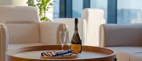 A modern living room with a round wooden table, two white sofas, a bottle of champagne, two glasses, and a tray with snacks.
