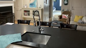 A modern kitchen with a black countertop, stainless steel sink, and a built-in oven. There is a dining area with a table and chairs, and a living room with a sofa and a coffee table. - Entire condo center of downtown Newburyport (Newburyport)