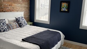 A bedroom with a white bed, blue walls, a brick accent wall, and a patterned rug. - Entire condo center of downtown Newburyport (Newburyport)