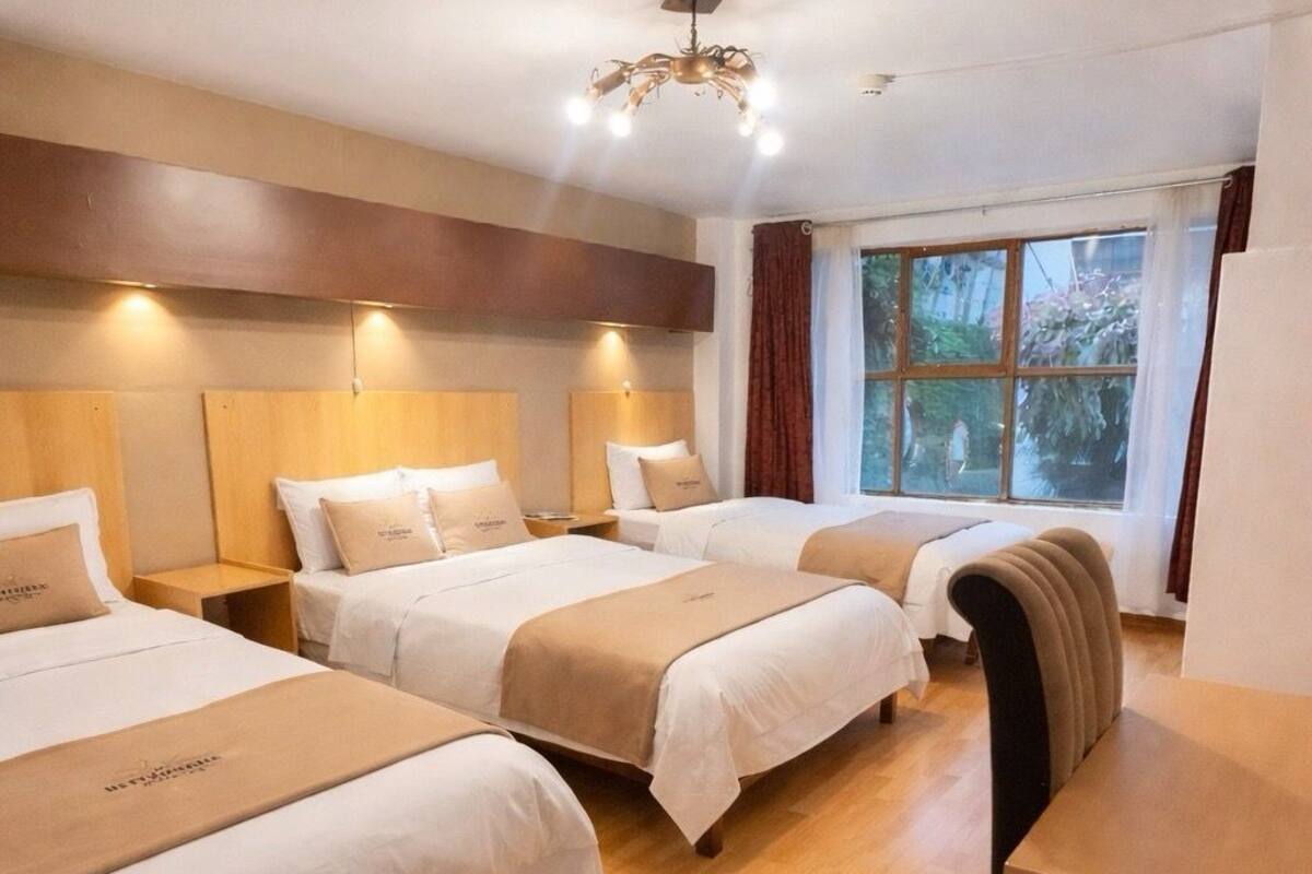 A hotel room with three beds, a desk, and a large window with curtains.
