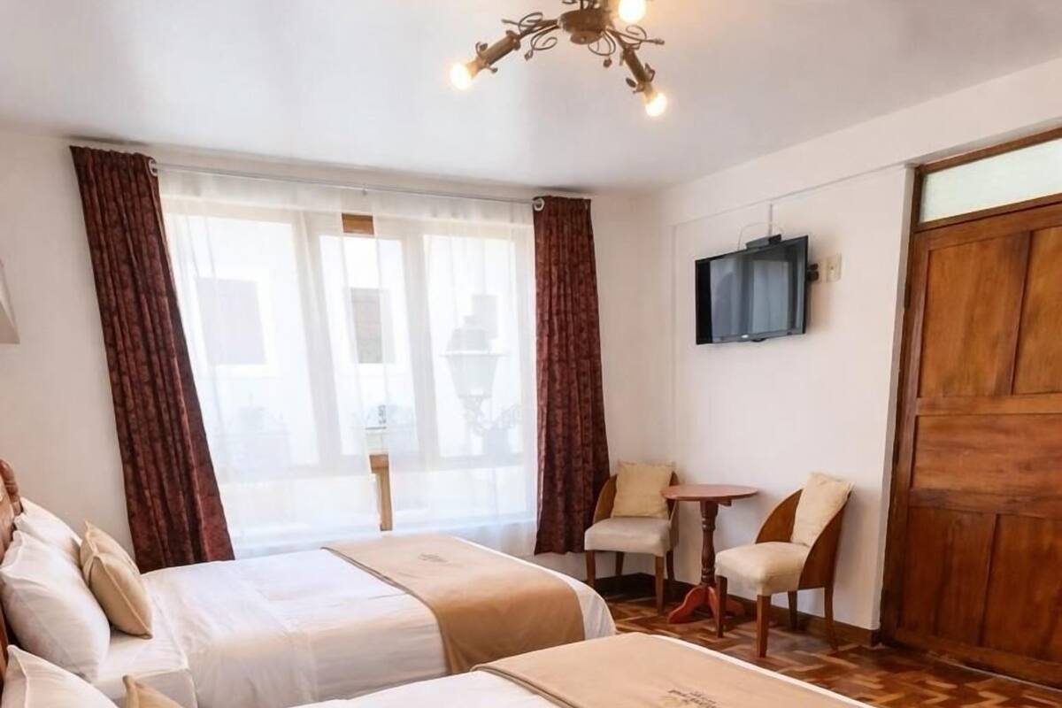 A hotel room with two beds, a TV, a wooden door, and a small table with chairs.