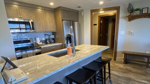 Una cocina moderna con encimera de mármol, electrodomésticos de acero inoxidable y taburetes de madera.