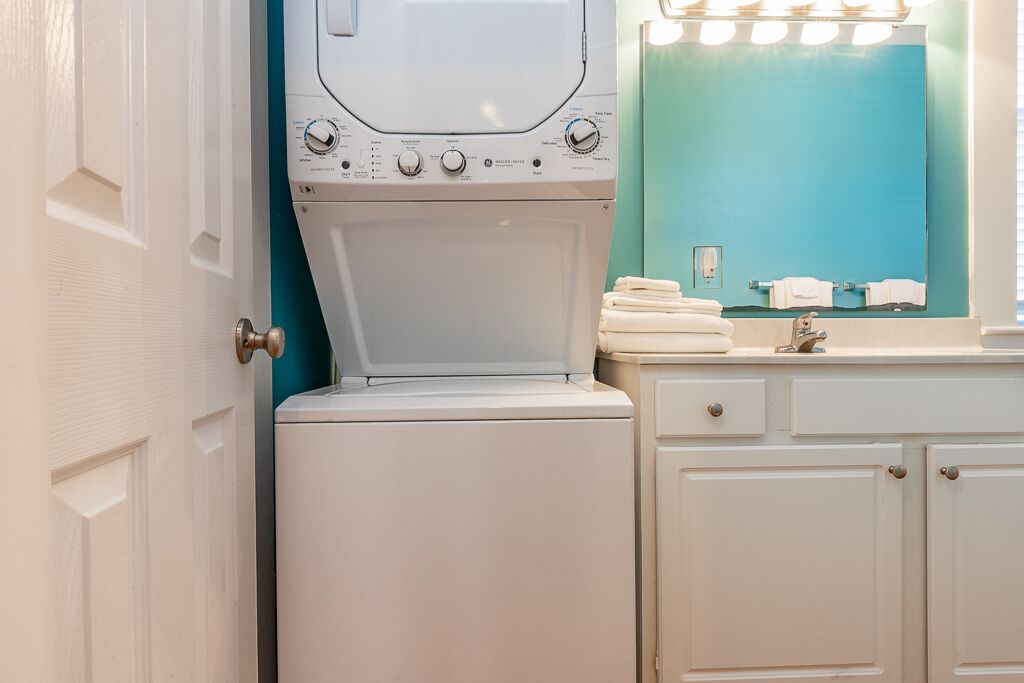Une salle de bain moderne et compacte, avec un lave-linge blanc, un lavabo avec un miroir et un mur d’accent de couleur turquoise.