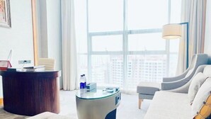 Une chambre d’hôtel moderne dotée d’une grande fenêtre, d’une table basse ronde en verre, d’un canapé, d’une table d’appoint et d’un bureau en bois.