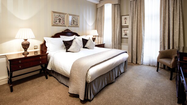 A hotel room with a large bed, two bedside tables with lamps, a chair, and a dresser. - 2-nights accommodation at 1-Bedroom Executive Residence in London (London)