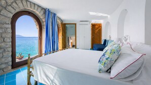 Ein Schlafzimmer mit einem großen Bett, einem Fenster in Form eines steinernen Bogens und Blick auf das Meer.