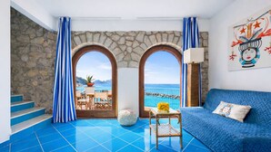 Ein Zimmer mit blau gefliestem Boden, einem blauen Sofa und zwei Bogenfenstern mit Blick auf das Meer.