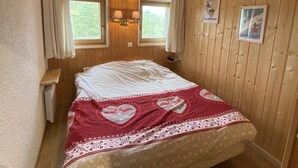 Ein Schlafzimmer mit Holzvertäfelung, einem Bett mit rot-weiß gestreifter Bettdecke, zwei Nachttischlampen und zwei gerahmten Bildern an der Wand.