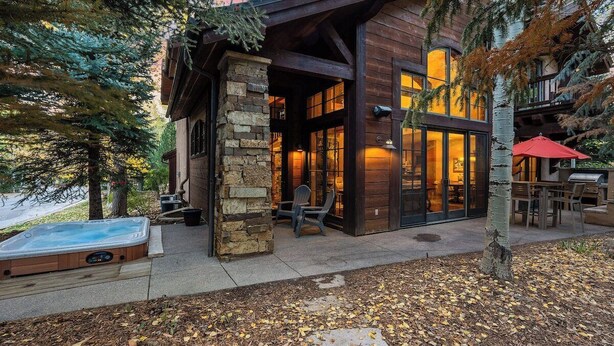 Una cabaña moderna de troncos con fachada de piedra, ventanas amplias y un jacuzzi al frente.