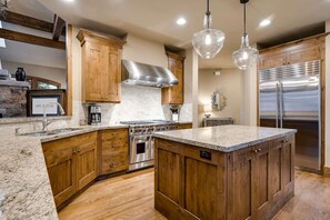 A kitchen with wooden cabinets, a stainless steel range hood, a built-in oven, and a large island with a granite countertop.