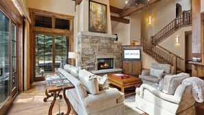 Un salón amplio con chimenea de piedra, un gran sofá y una escalera que sube a un nivel superior.
