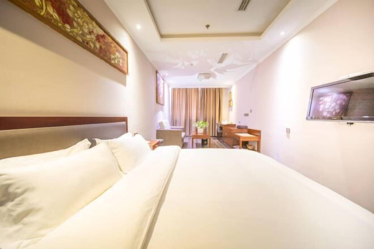 Une chambre d’hôtel avec un grand lit, un bureau, une chaise, une télévision et une fenêtre avec des rideaux.