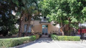 A building with a central entrance, surrounded by well-maintained greenery and a paved pathway leading to the door.