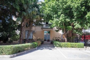 A building with a central entrance, surrounded by well-maintained greenery and a paved pathway leading to the door.