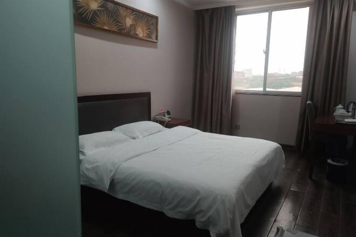 Une chambre d’hôtel comprenant un lit, une table de chevet, un bureau, une fenêtre avec des rideaux et une œuvre d’art murale.