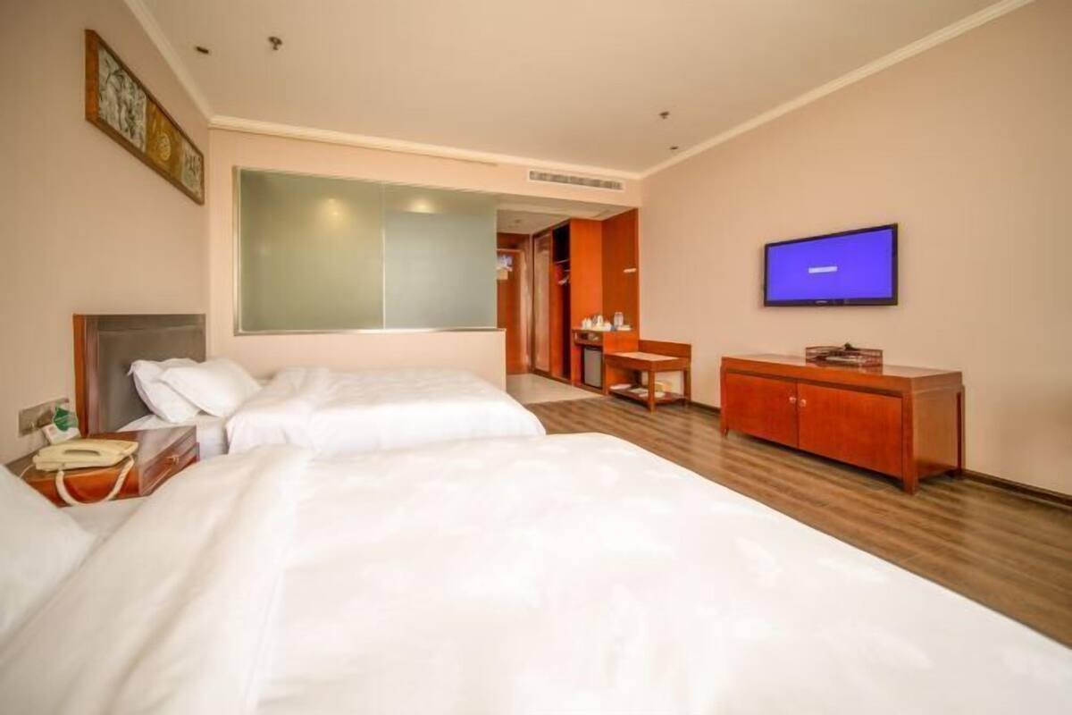 Une chambre d’hôtel avec deux lits, une télévision, une armoire en bois et un bureau.