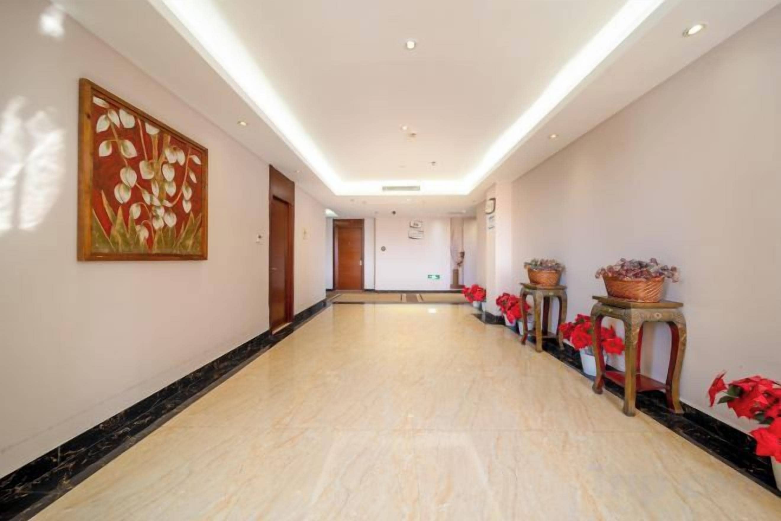 A hotel corridor with a marble floor, a painting on the wall, and potted plants.