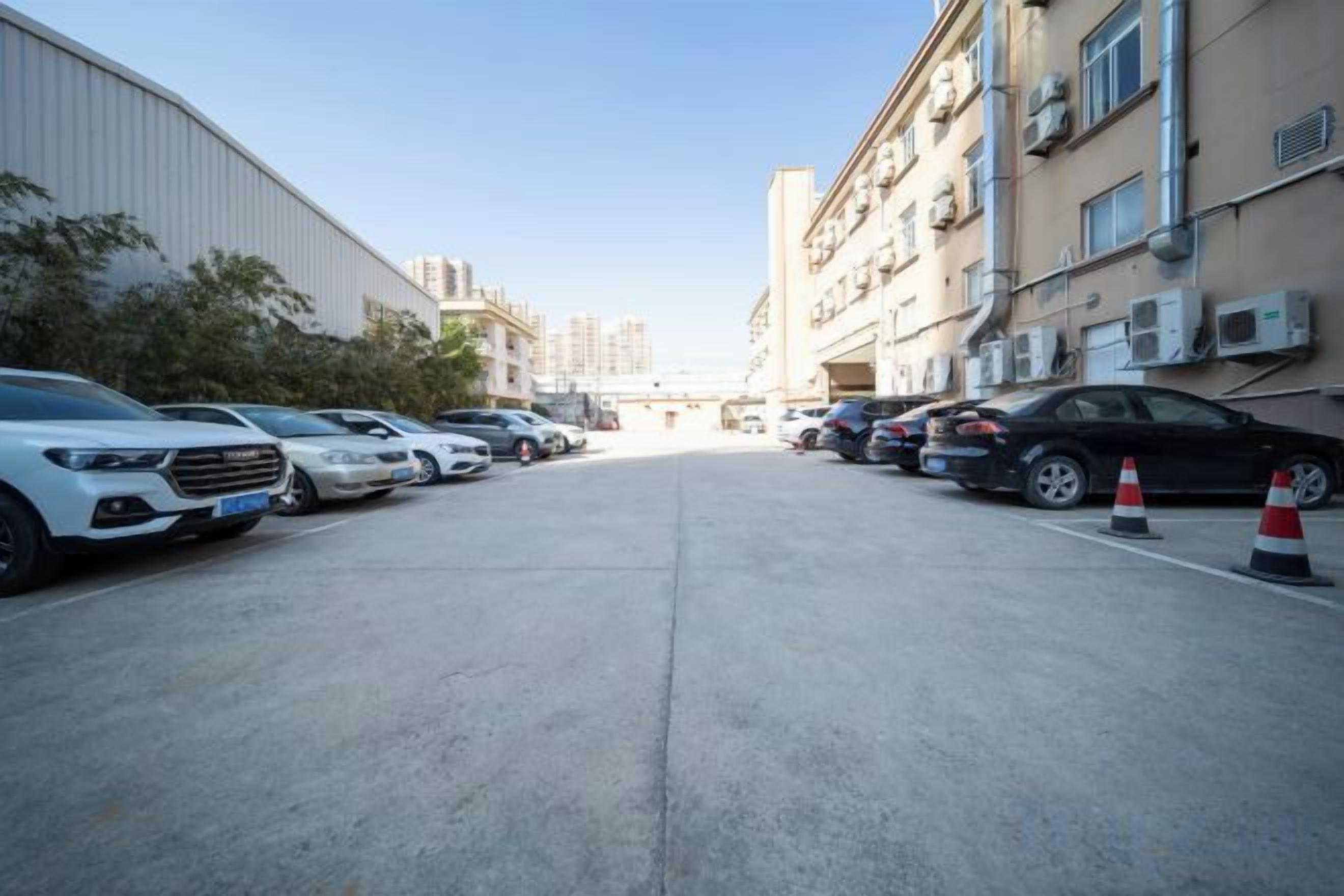 A parking lot with multiple cars parked in rows, a building with air conditioning units, and a clear sky.