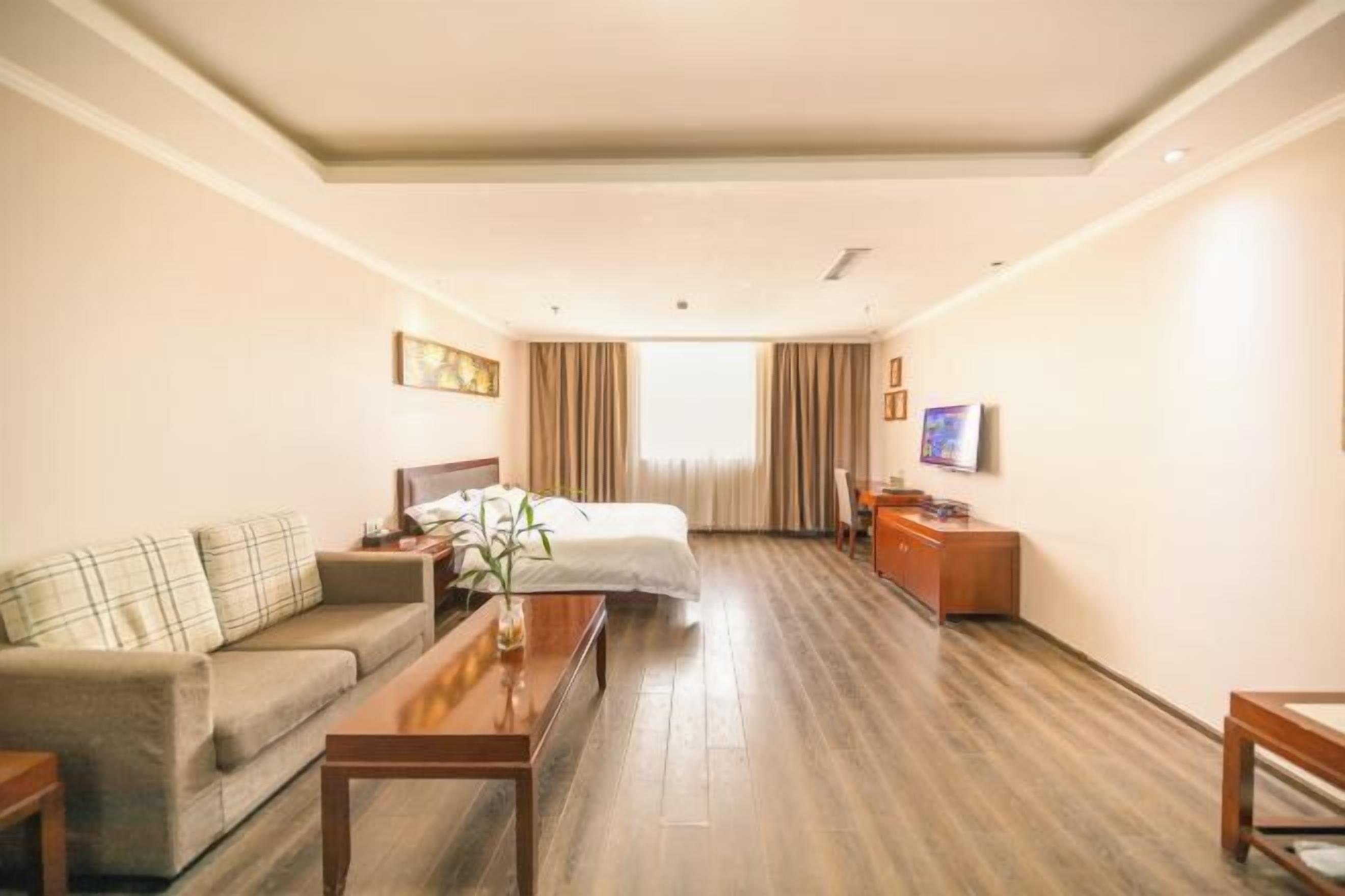 A hotel room with a bed, a sofa, a desk, a TV, and a window with curtains.