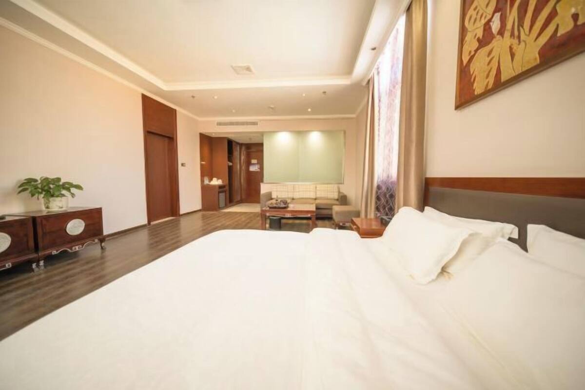 Une chambre d’hôtel avec un grand lit, un bureau, une chaise, un canapé et une plante en pot.
