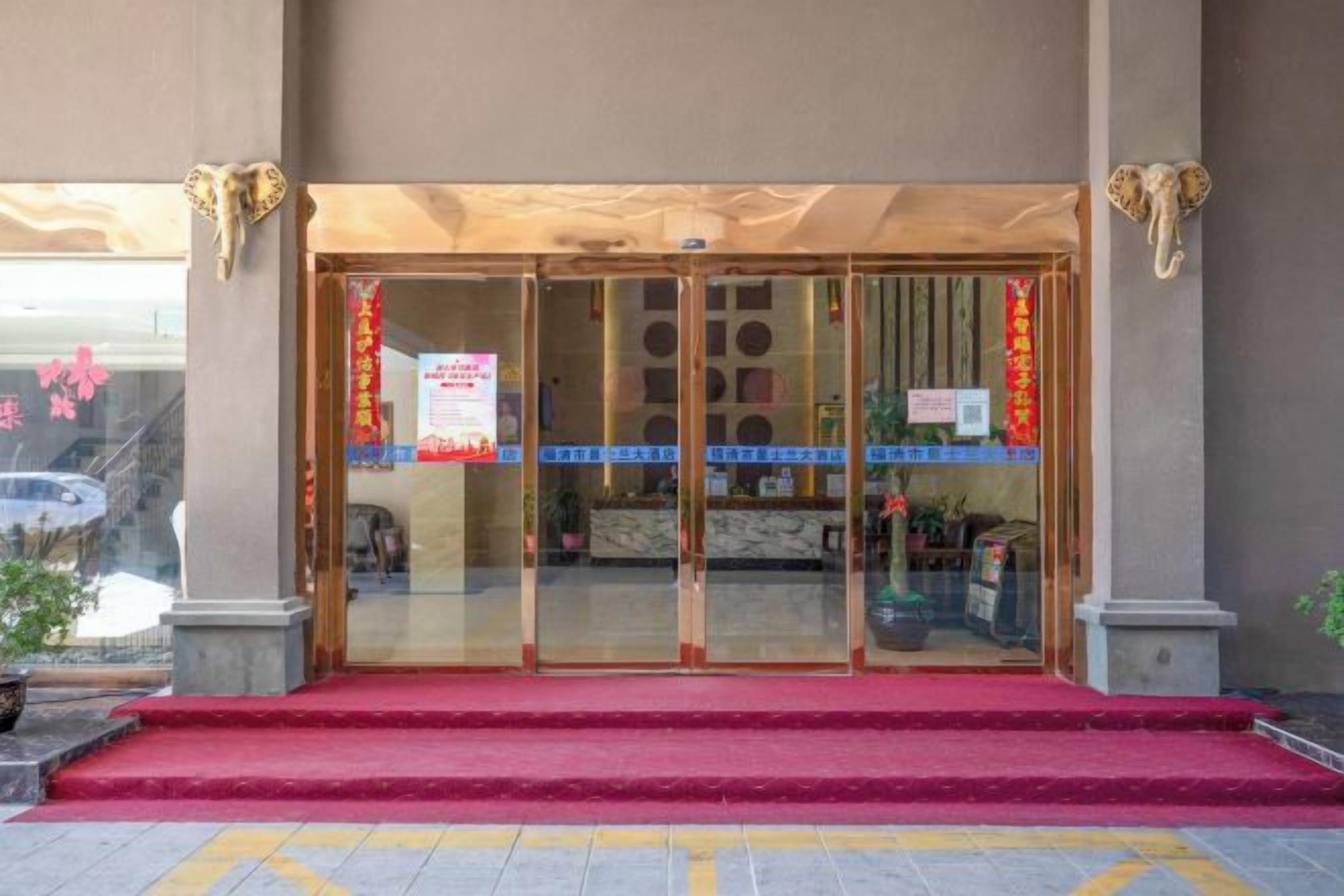 Entrada de hotel con alfombra roja, puertas de vidrio y un cartel.