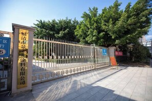 A gated entrance with a metal fence, a signboard, and a tree in the background.
