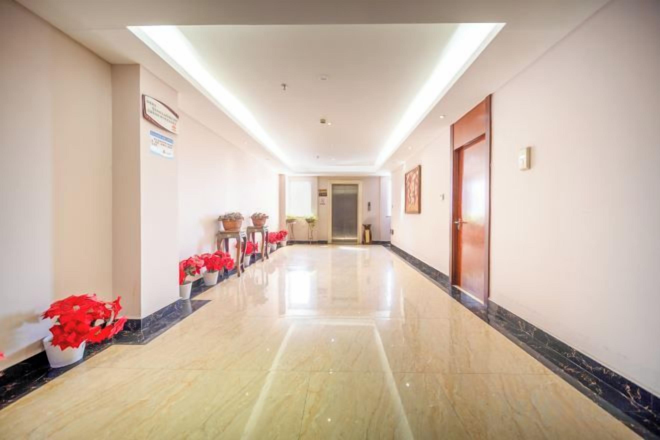 A hotel corridor with a polished floor, potted plants, and a door at the end.