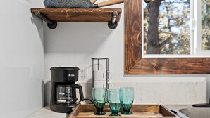 Een keuken met een koffiezetapparaat, een dienblad met glazen en een houten plank boven het aanrecht.