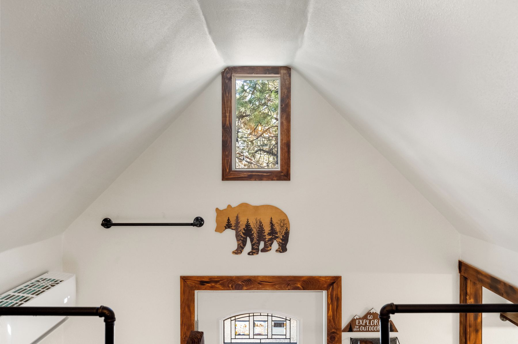 A room with a sloped ceiling, a window with a view of trees, a wooden bear decoration, a framed picture, and a wooden door with a sign.