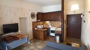 Una cucina compatta con TV, pensili in legno, lavello e piano cottura.