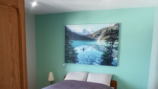 Una camera da letto con un letto, un armadio in legno, un comodino, una lampada e un dipinto che raffigura un paesaggio montano.