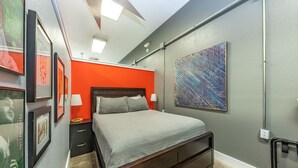 A bedroom with a bed, a nightstand, a lamp, a painting, and a ceiling fan.
