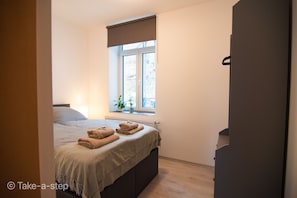 Um quarto com cama, janela com vista, radiador e planta no parapeito.