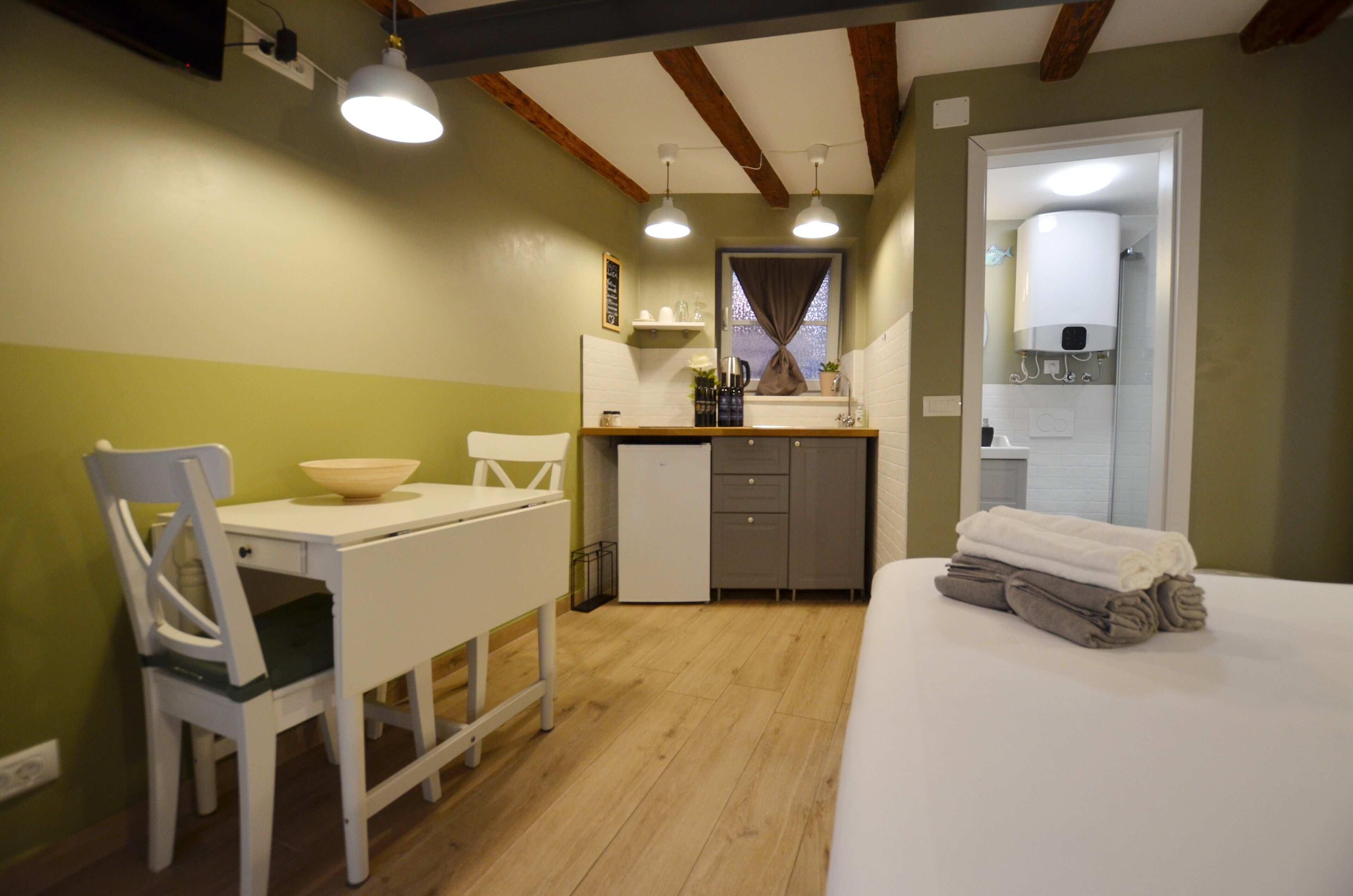 Una habitación compacta con cama, una pequeña mesa con sillas, kitchenette y baño.