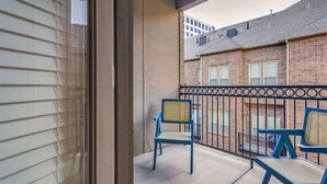 A balcony with two chairs and a table, a brick building in the background, and a window with blinds.