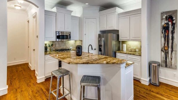 A modern kitchen with white cabinetry, a granite countertop, stainless steel appliances, and two bar stools.
