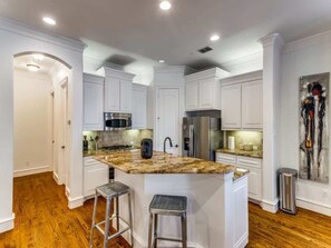 A modern kitchen with white cabinetry, a granite countertop, stainless steel appliances, and two bar stools.