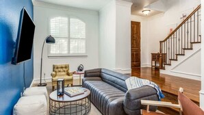 A living room with a sectional sofa, a round coffee table, a TV mounted on the wall, and a staircase leading to another level.