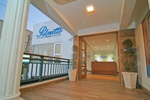 L’entrée d’un hôtel avec un comptoir d’accueil, un balcon doté d’une balustrade et des plantes en pot.