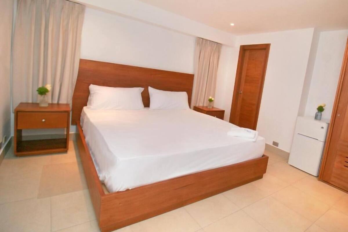 Une chambre d’hôtel avec un lit en bois, deux tables de chevet, une armoire et une porte.