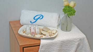 Een badkamer met een witte handdoek met een monogram, een schotel met verzorgingsproducten en een vaas met bloemen.