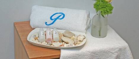 Un baño con una toalla blanca con un monograma, un plato de productos de baño y un jarrón con flores.
