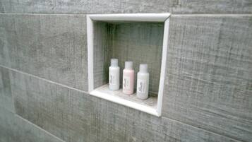 Un baño con un estante que contiene cuatro botellas de artículos de aseo.