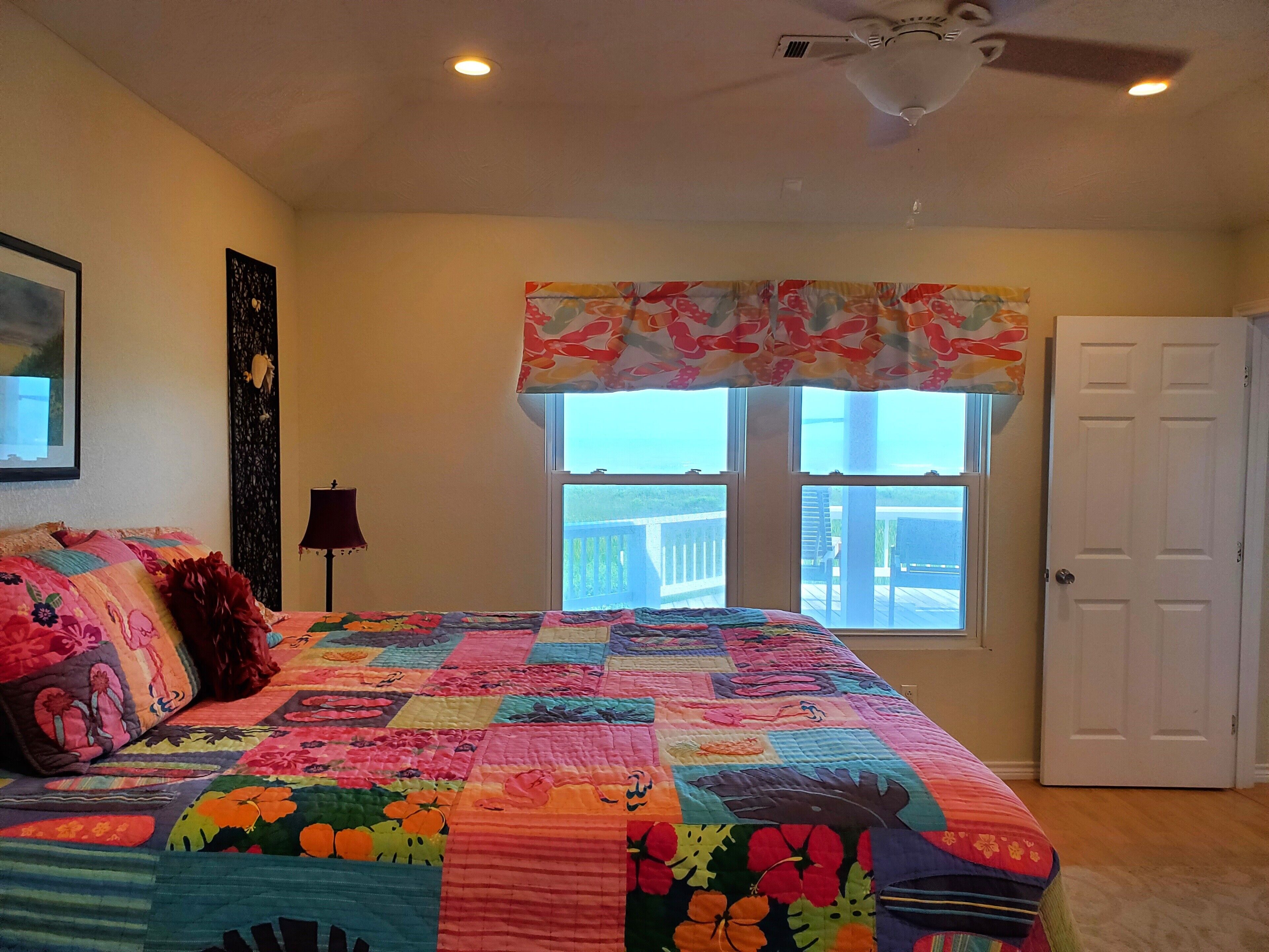 Une chambre avec un grand lit, un ventilateur de plafond, une fenêtre donnant sur un beau paysage et une porte.