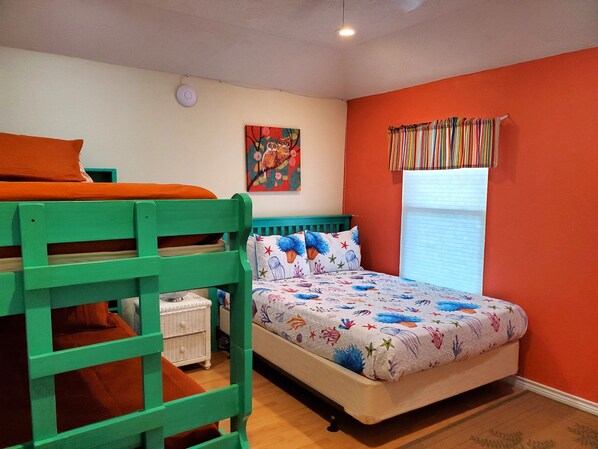 Un dormitorio con una cama litera, una cama individual con colcha de colores con motivos marinos, una ventana con cortinas a rayas y un cuadro de lechuzas colgado en la pared.